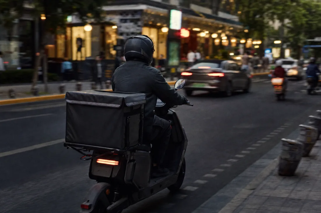 A food delivery rider on an electric scooter moving through a Chinese city street at dusk